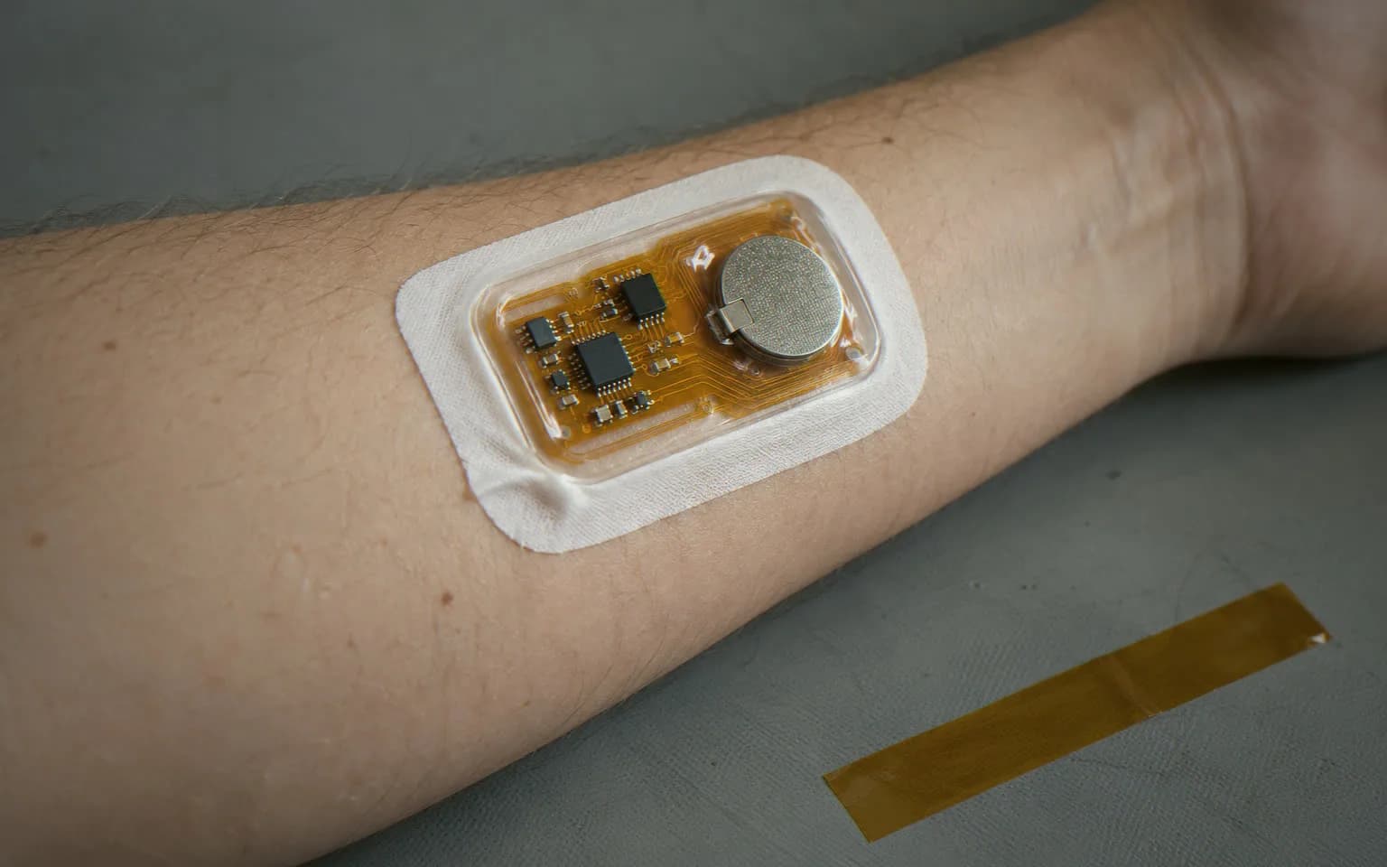 Flex circuit health patch sealed in clear silicone, stuck on a forearm
